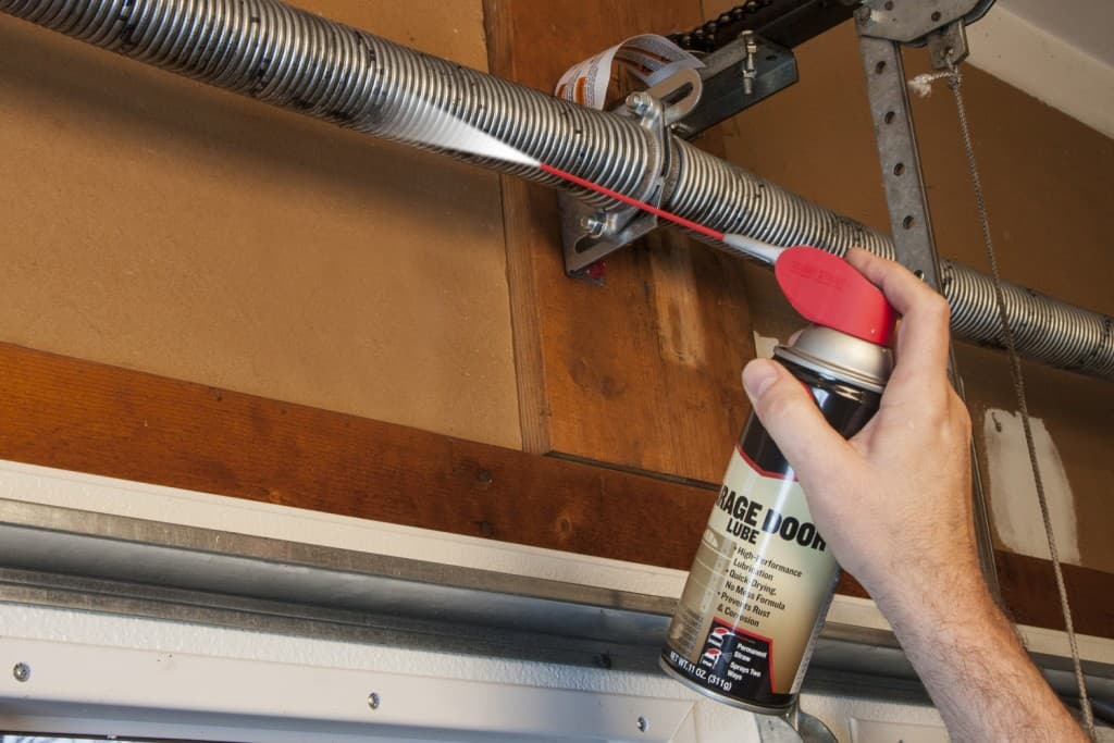 Technician lubricating garage door torsion spring